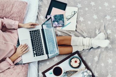 Pijamalı genç bir kadının evde yatarken dizüstü bilgisayar kullanmasını yakından izle.