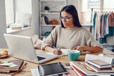 İçerde çalışırken dizüstü bilgisayar kullanan gündelik giysili güzel bir kadın. 