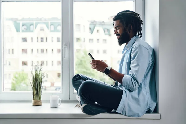 Happy Young African Man Using Smartphone Smiling While Sitting Window — Stock Photo, Image