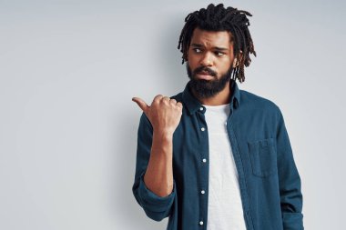 Gri arka planda dikilirken fotokopi alanını gösteren gündelik giysili ciddi bir Afrikalı genç adam.