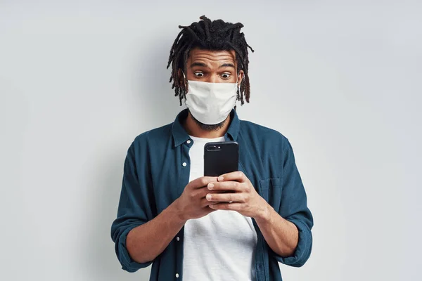 Sorprendido Joven Africano Con Máscara Facial Médica Uso Teléfono Inteligente —  Fotos de Stock