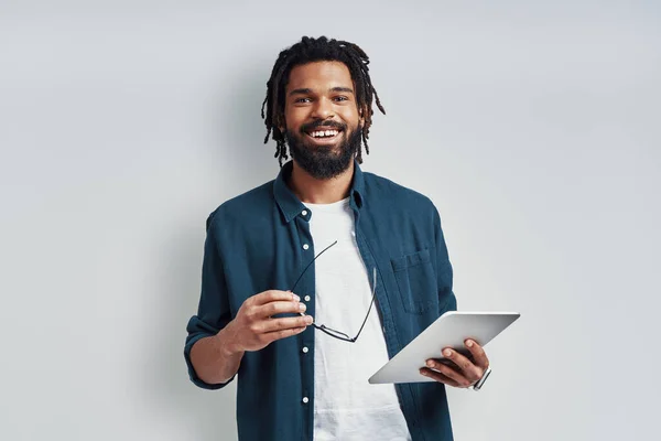 身穿休闲装的聪明的非洲年轻人 站在灰色背景下 用数码平板电脑微笑着 — 图库照片