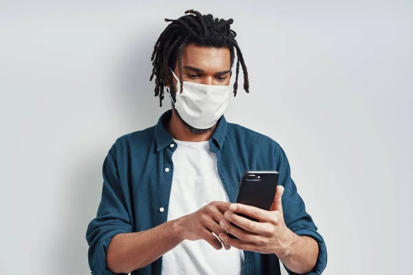 Careful Young African Man Wearing Medical Face Mask Using Smartphone — Stock Photo, Image