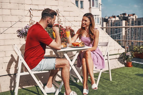 屋上のパティオの屋外に座っている間 朝食と笑顔を持つカジュアルな服でかわいい若いカップル — ストック写真