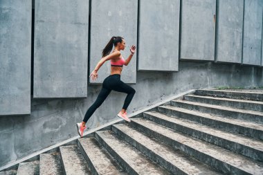 Spor elbiseli genç bir kadın merdivenlerde spor yaparken tam boy koşuyor.