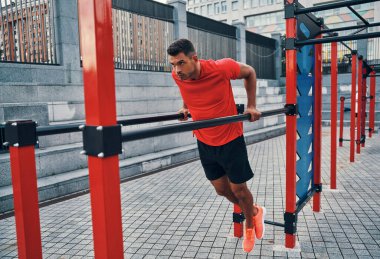 Spor elbiseli güçlü bir genç adam şehir caddesinde barfiks çekerken egzersiz yapıyor.