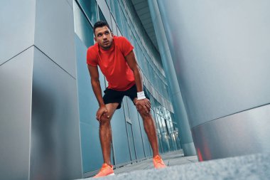 Spor kıyafetleri içinde uzun boylu genç bir adam spor yaparken dışarıda egzersiz yapıyor.