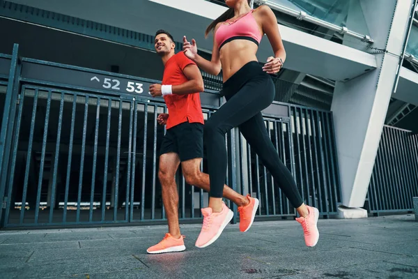 Full length of fit and beautiful young man and woman in sports clothing running while practicing outdoors