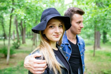 Güzel, gülümseyen bir kadın kameraya bakarken erkek arkadaşı da parka bakıyor. 