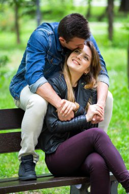 Genç bir adam bankta oturuyor ve sevgilisini alnından öpüyor.