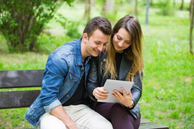 Park bankında dijital tablet kullanan genç çift