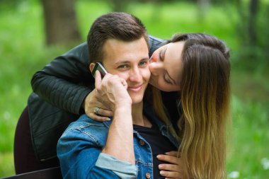 Gülümseyen yakışıklı adamlar telefonda konuşuyor ve kadın parkta yanağını öpüyor. 