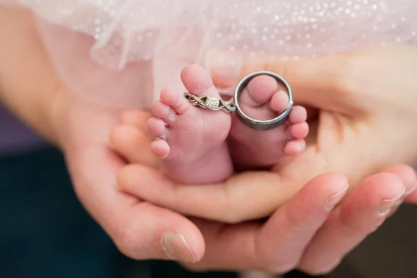 Anillos de boda en los pies del bebé recién nacido con las manos de los padres sosteniendo —  Fotos de Stock