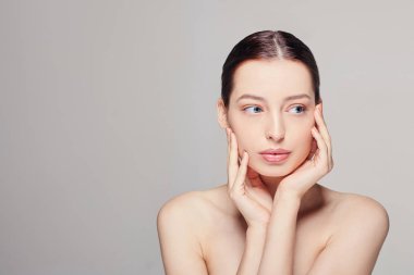İki eliyle yüzüne dokunan taze ve temiz ciltli güzel bir genç kadın. Spa, kozmetoloji ve güzellik.