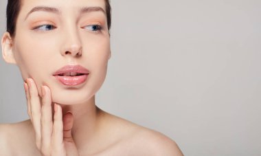 Temiz tenli güzel genç bir kadın sağ eliyle kendi yüzüne dokunuyor. Güzellik ve güzellik merkezi. Yüz bakımı.