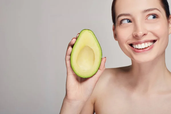 Profile side portrait of brown-haired attractive nude lady with perfect pure skin with avocado in the hand and smiling with teeth and looking at side — Stock Photo, Image