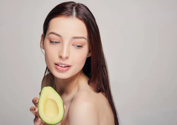 beautiful tender brown-haired nude lady with perfect pure shine skin with avocado in the hand
