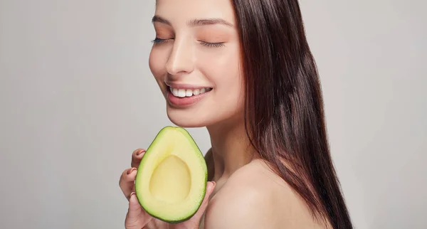 Happy lady with perfect pure shine skin with avocado in the hand and smiling with teeth — Stock Photo, Image