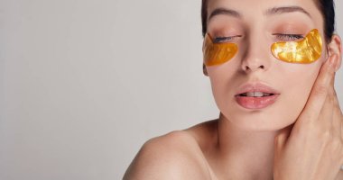 Kozmetik prosedürleri. Yüz bakımı. Genç ve güzel bir kız gözlerinin altına altın kolajen bantları yapıştırıyor. Kırışıklıkları ve koyu halkaları yok et. Bir kadın gözlerinin etrafında narin bir ciltle ilgilenir..