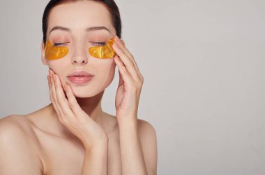 Yüz bakımı. Dümdüz. Gözlerinin altına altın kolajen bantları yapıştıran genç bir kız. Kırışıklıkları ve koyu halkaları sil.