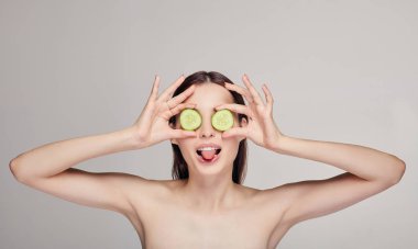 Koyu saçlı, dolgun dudaklı ve neşeli bir havası olan güzel ve çekici bir genç bayan. Kız salatalık dilimlerinden gözlük yaptı ve dilini çıkardı. Orta çerçeve.