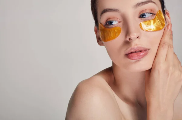 Menina bonita jovem aplicando manchas de colágeno dourado sob os olhos dela. Remova rugas e olheiras . — Fotografia de Stock