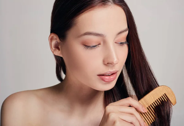 Close up a tender girl with a playful mood combs her hair with a light brown comb on the background looks