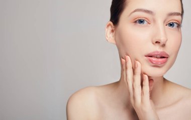 Temiz ve taze tenli güzel genç bir kadın sağ eliyle yüzüne dokunuyor. Kozmetik, güzellik ve kaplıca.