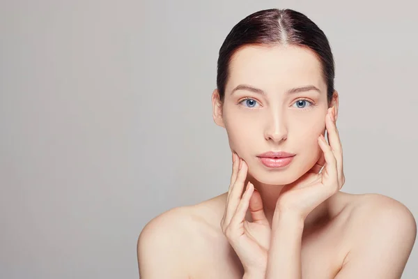 İki eliyle yüzüne dokunan temiz tenli bir kadın. Dümdüz. Spa, kozmetoloji ve güzellik.