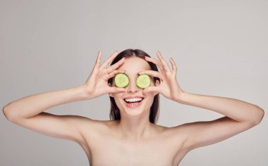 Güzel, çekici, saçları dolgun dudaklı ve neşeli bir genç bayan. Kız salatalık dilimlerinden gözlük yaptı ve beyaz dişlerle gülümsedi. Spa, kozmetik. Orta çerçeve