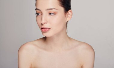 Mavi gözlü ve dolgun dudaklı, sevimli, genç bir kız. Gri arka plan. Kahverengi saçlı. Gülümseyerek yana bakıyor. Boşluğu kopyala.