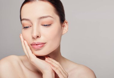 Dolgun dudaklı, koyu renk saçlı ve gri arka planda parlak, narin bir teni olan kültürlü bir kız. Bayan eliyle yüzüne dokunuyor. Tarafıma bakıyorum. Cilt bakımı, kozmetoloji. Zindelik.