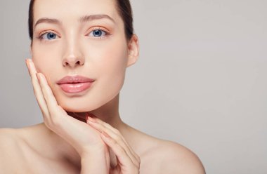 Şehvetli, güzel, kahverengi saçlı, temiz tenli, çıplak omuzlu, gri stüdyo arka planında poz veren yüzüne dokunan, açık renk, çıplak makyajlı, fotokopi çeken bir kız.