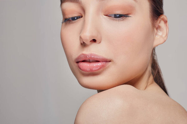 Young beautiful pritty girl with blue eyes and full lips. Grey background. Dark hair. Looking down. Copy space. Spa, cosmetology.