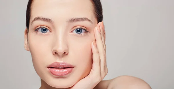 Una chica hermosa sofisticada excelente con labios, cabello oscuro y piel delicada limpia radiante en el fondo gris. La señora puso su cabeza en su mano. Se ve recto. Cosmetología —  Fotos de Stock