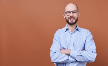 Yakışıklı genç bir adam, kel, sakallı, yuvarlak gözlüklü ve çizgili gömlekli bir iş adamı, kollarını göğsünde kavuşturdu ve düz görünüyordu. Mutlu ve başarılı iş adamının yüzüne yakın çekim..