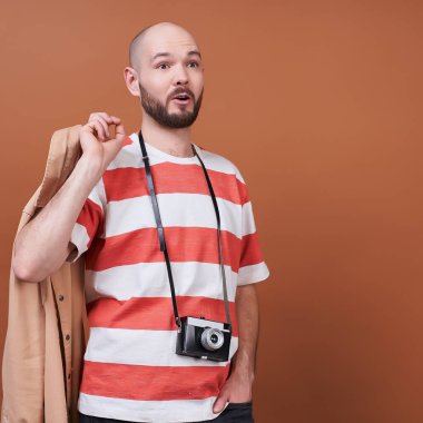 Kahverengi gözlü, çizgili tişörtlü, genç ve yakışıklı bir adam gömleğini omzunun üzerinden fırlattı ve hayranlıkla yan tarafına baktı. Fotoğraf kahverengi, çıplak arkaplanda..