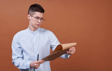 Koyu renk saçlı, gözlüklü ve mavi gömlekli yakışıklı bir genç. Kayıt için sarışını tutuyor. Programı kontrol ediyor, günün programını izliyor..