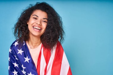 Amerika 'yı seviyorum. Gülümseyen, çekici, kıvırcık saçlı bir Afrikalı omuzlarındaki Amerikan bayrağını gösteriyor, mavi bir arka planda yalıtılmış..