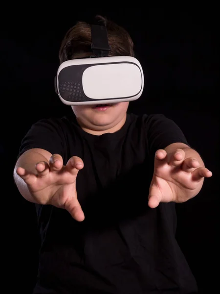 Sanal gerçeklik gözlüğü takan çocuk elleriyle bir şey tutuyor, siyah arka planda izole edilmiş..
