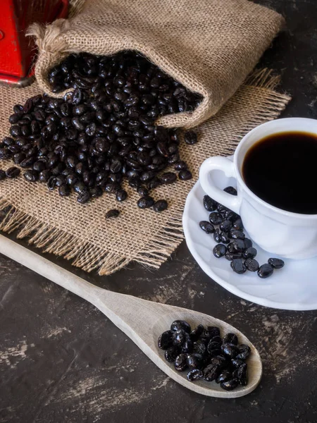 Tasse und Beutel mit Kaffeebohnen aus der Tüte auf dem Steintisch und Holzlöffel — Stockfoto