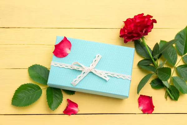 A blue gift box with a white ribbon and a red rose on a yellow wooden background. Concept of Valentine\'s day, a romantic gift. Copy space for text.