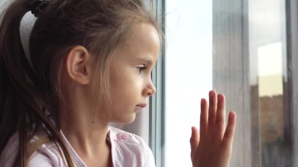窓際の小さな悲しい女の子の肖像画 悲しい子ビデオ 窓の外に見える — ストック動画