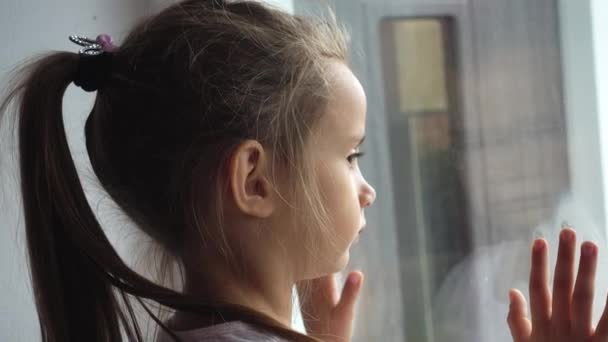 窓際の小さな悲しい女の子の肖像画 悲しい子ビデオ 窓の外に見える — ストック動画
