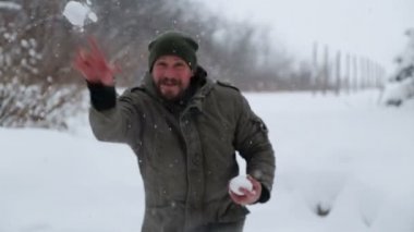 Kışın kartopu oynayan bir adam. Sakallı erkek bir kartopu kameraya doğru atar..