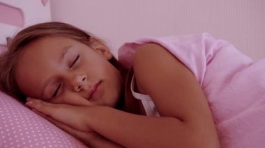 Küçük kız pembe bir yatakta uyuyor. Yatakta sabah uyanan bir bebeğin portresi.
