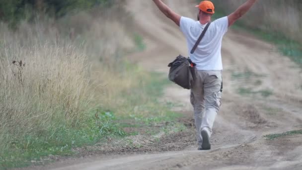 村の道でヒッチハイクをしている男 若いあごひげの男が野原で車を止める 旅行仲間 旅行者 放浪者 — ストック動画