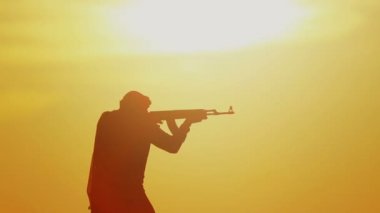 Günbatımında Kalaşnikof ile İslam savaşçısı. Müslüman savaşçı gün batımında makineli tüfekle antrenman yapıyor.. 