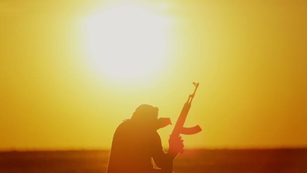 Islamischer Krieger mit Kalaschnikow am Tag des Sonnenuntergangs. Muslimischer Kämpfer trainiert bei Sonnenuntergang mit einem Maschinengewehr. 