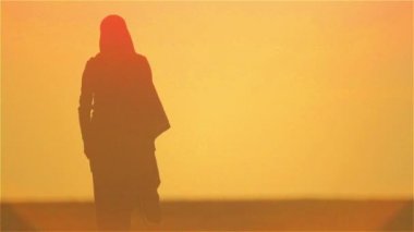 Çölde yalnız duran Arap bir kadının silueti. Arap kız gün batımı silueti.